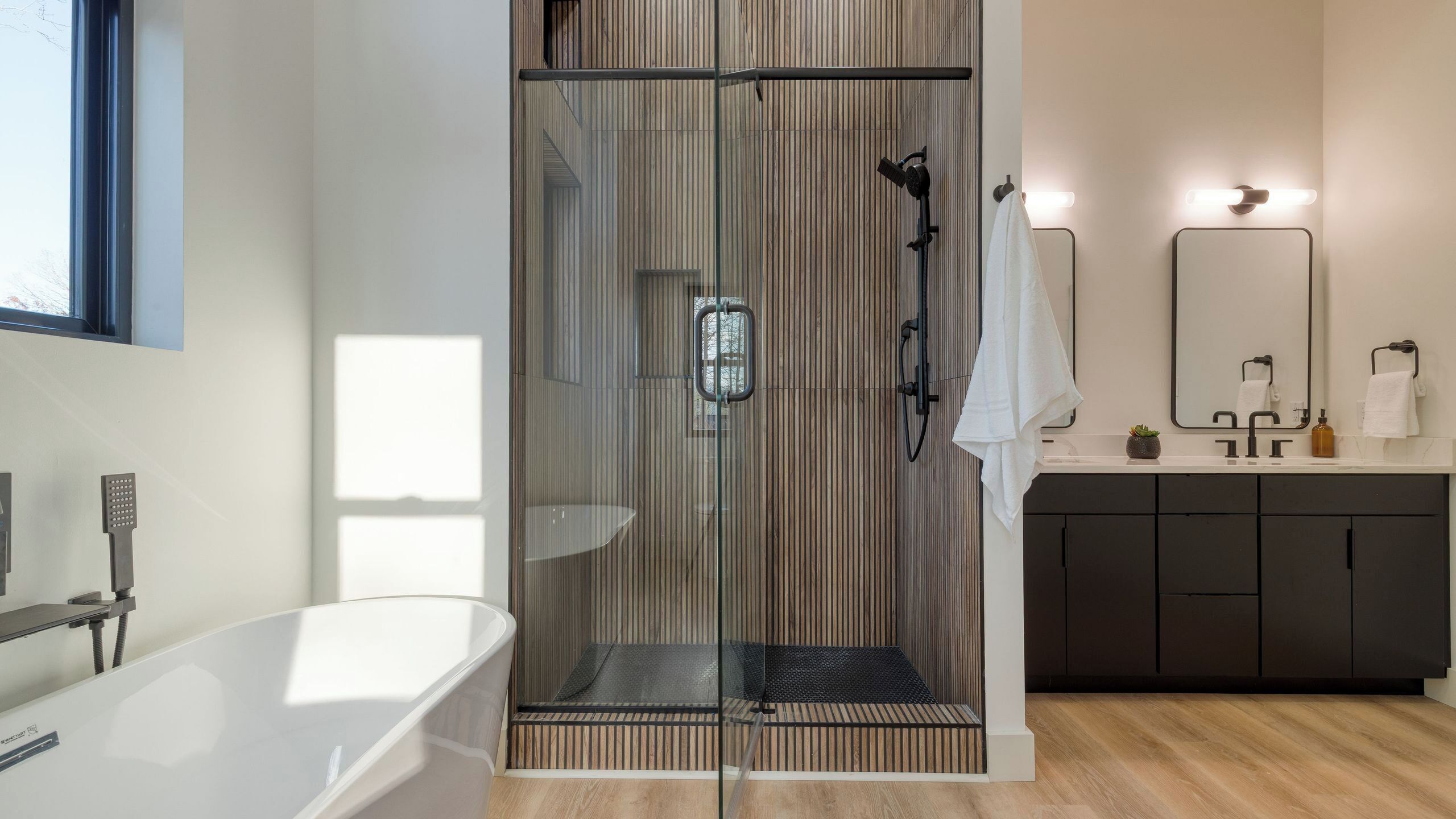 A modern bathroom with a glass-enclosed shower, a freestanding bathtub, and a vanity with a mirror.