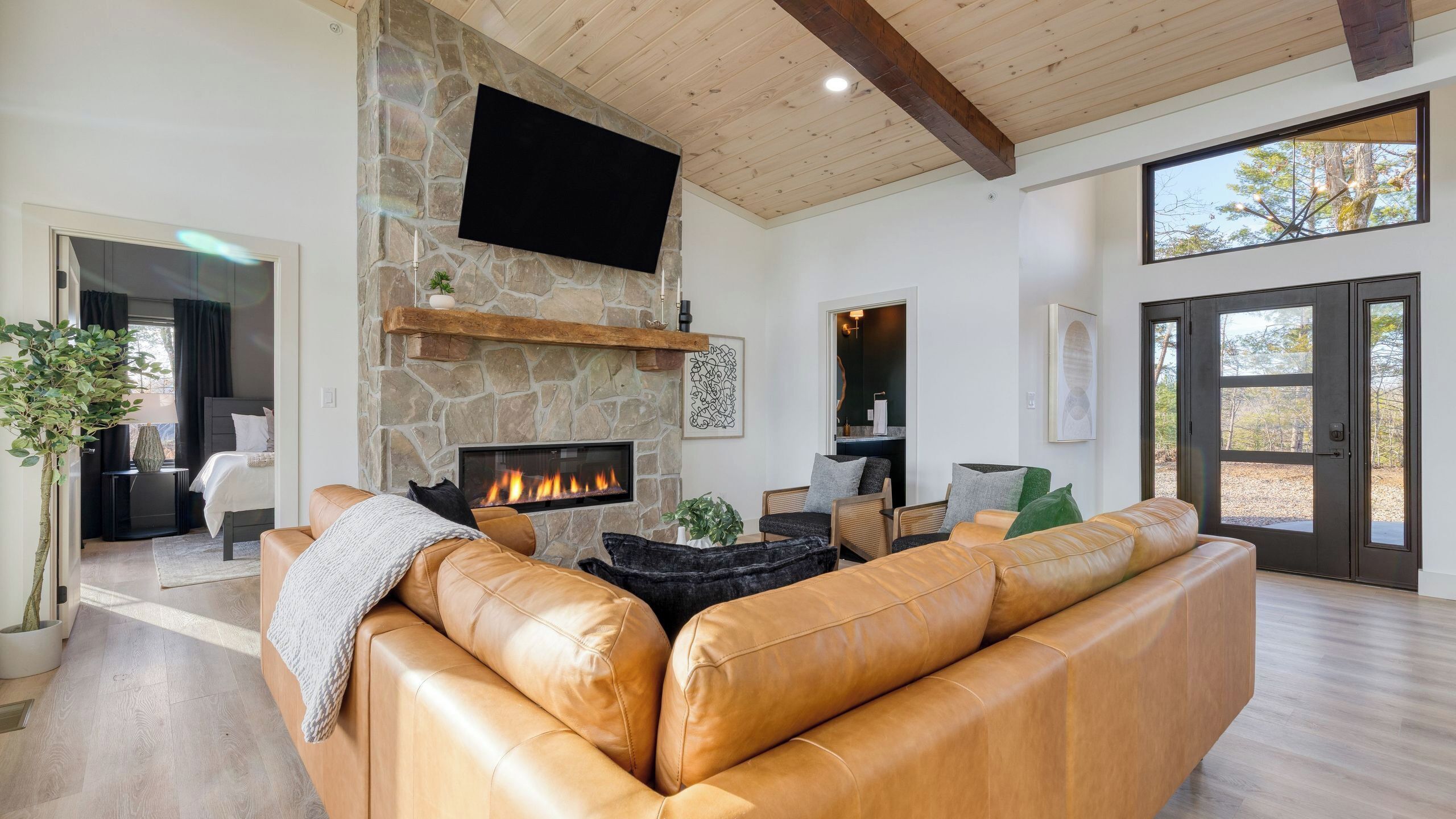 A modern living room with a stone fireplace, leather sofa, and a flat-screen TV.