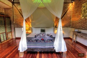 A four-poster canopy bed with a heart-shaped swan decoration, a wooden bench, and a brick wall with a mural. - Villa Samalama Gili Air (Pemenang)