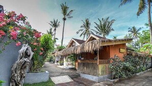 A traditional thatched-roof house with a small porch, surrounded by lush greenery and palm trees. - Villa Samalama Gili Air (Pemenang)