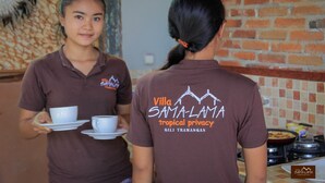 Two individuals in brown shirts with 'Villa Samaluma tropical privacy' printed on the back, serving coffee in a restaurant setting with a brick wall and tiled backsplash. - Villa Samalama Gili Air (Pemenang)