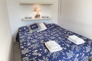 A bed with a nautical-themed bedspread, a bedside lamp, and a shelf with decorative items. - Alassio Centre, Ideal for Families (Alassio)