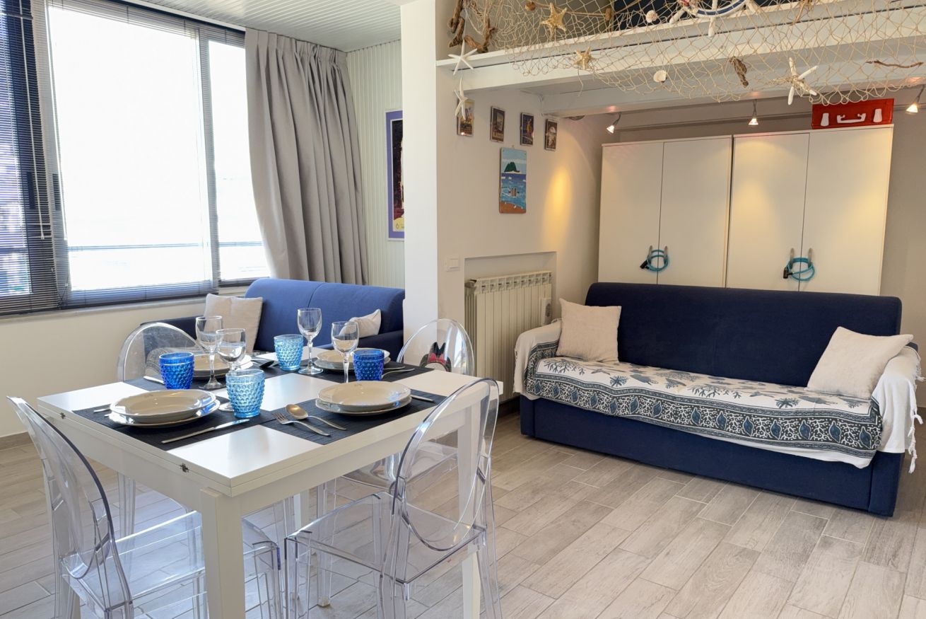 A room with a dining table set for two, a sofa, and a bed.