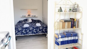 Ett sovrum med en säng, ett nattduksbord med en lampa, en vägghylla och en bokhylla i metall.