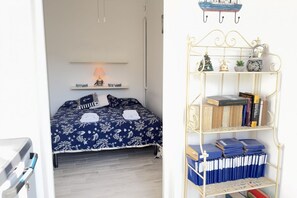 A bedroom with a bed, a bedside table with a lamp, a wall-mounted shelf, and a metal bookcase. - Alassio Centre, Ideal for Families (Alassio)
