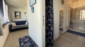Ett rum med en soffa, en bänk, en dörr med en gardin och en spegel på väggen.