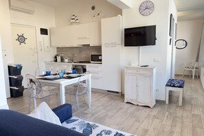 A compact kitchen with white cabinets, a dining table with chairs, a TV mounted on the wall, and a small seating area with a bench. - Alassio Centre, Ideal for Families (Alassio)