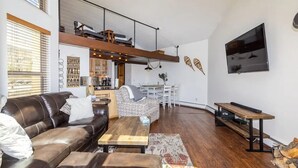 A modern living room with a brown leather sofa, a wooden coffee table, and a dining area with a white table and chairs. - Top Floor, End Unit Condo with Amazing Mountain Views (Silverthorne)