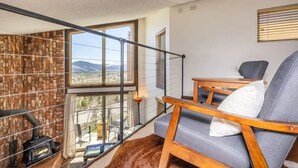 A cozy room with a large window, a wooden chair, a small table, and a fireplace. - Top Floor, End Unit Condo with Amazing Mountain Views (Silverthorne)