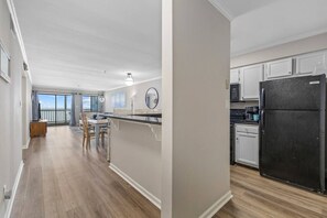 A modern kitchen with white cabinets, a black refrigerator, and a dining area with a view. - Garden City Beach Oceanfront Condo w/ Huge Balcony & Stunning Views! (Murrells Inlet)