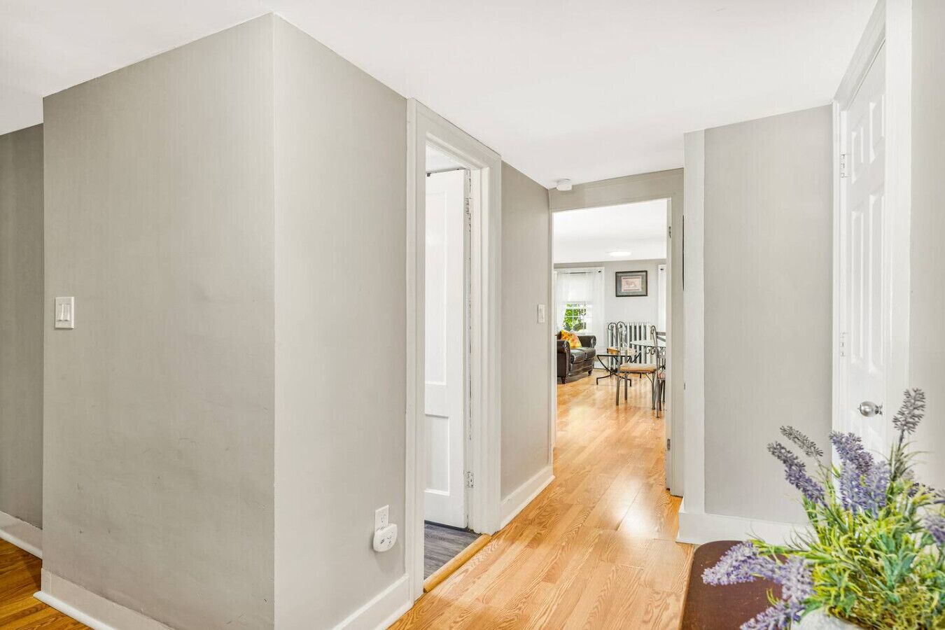 A hallway with grey walls and wooden flooring leading to a dining area with a table and chairs.