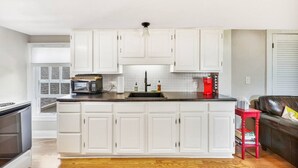 A modern kitchen with white cabinetry, a built-in microwave, a coffee maker, and a red stool. - SUNNY PRIVATE 1 BEDROOM APARTMENT (Portland)
