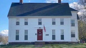 A two-story white house with a dark roof, a red door, and an American flag on the front. - SUNNY PRIVATE 1 BEDROOM APARTMENT (Portland)