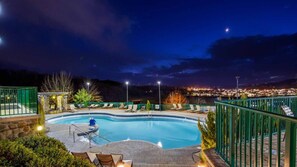 Une piscine éclairée la nuit, avec une vue sur le paysage urbain en arrière-plan.