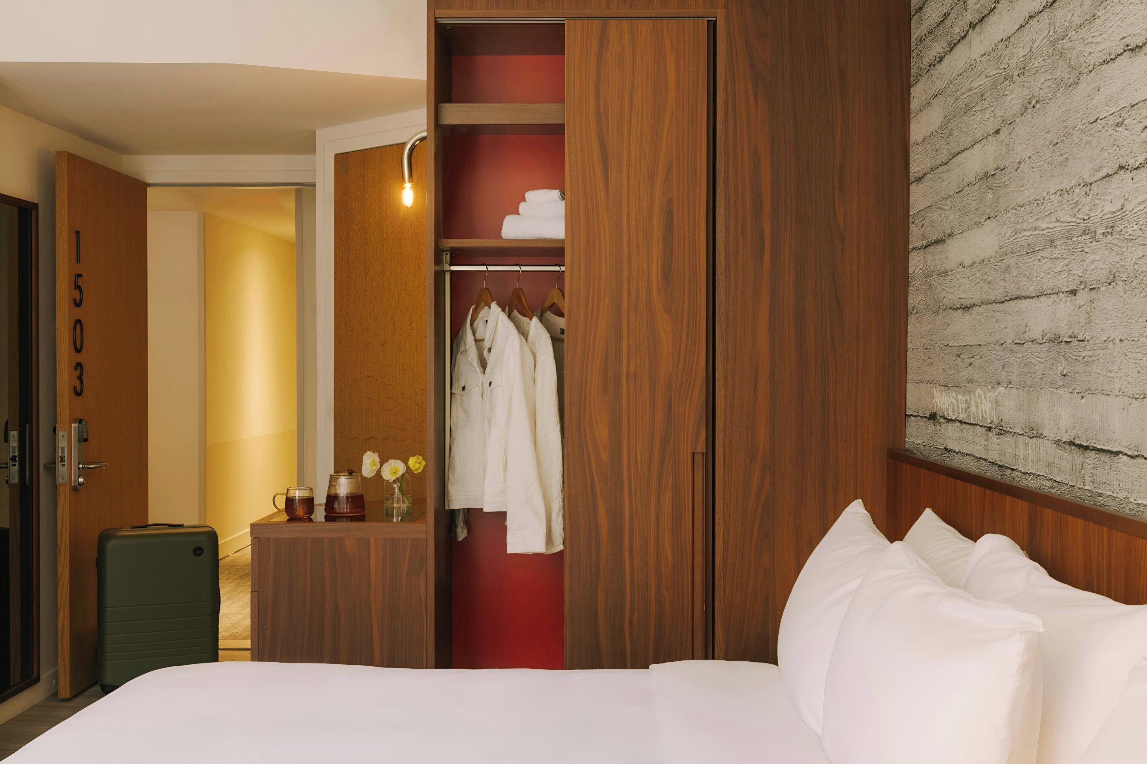 Una habitación de hotel con un armario de madera, una cama con ropa de cama blanca y una pared roja.
