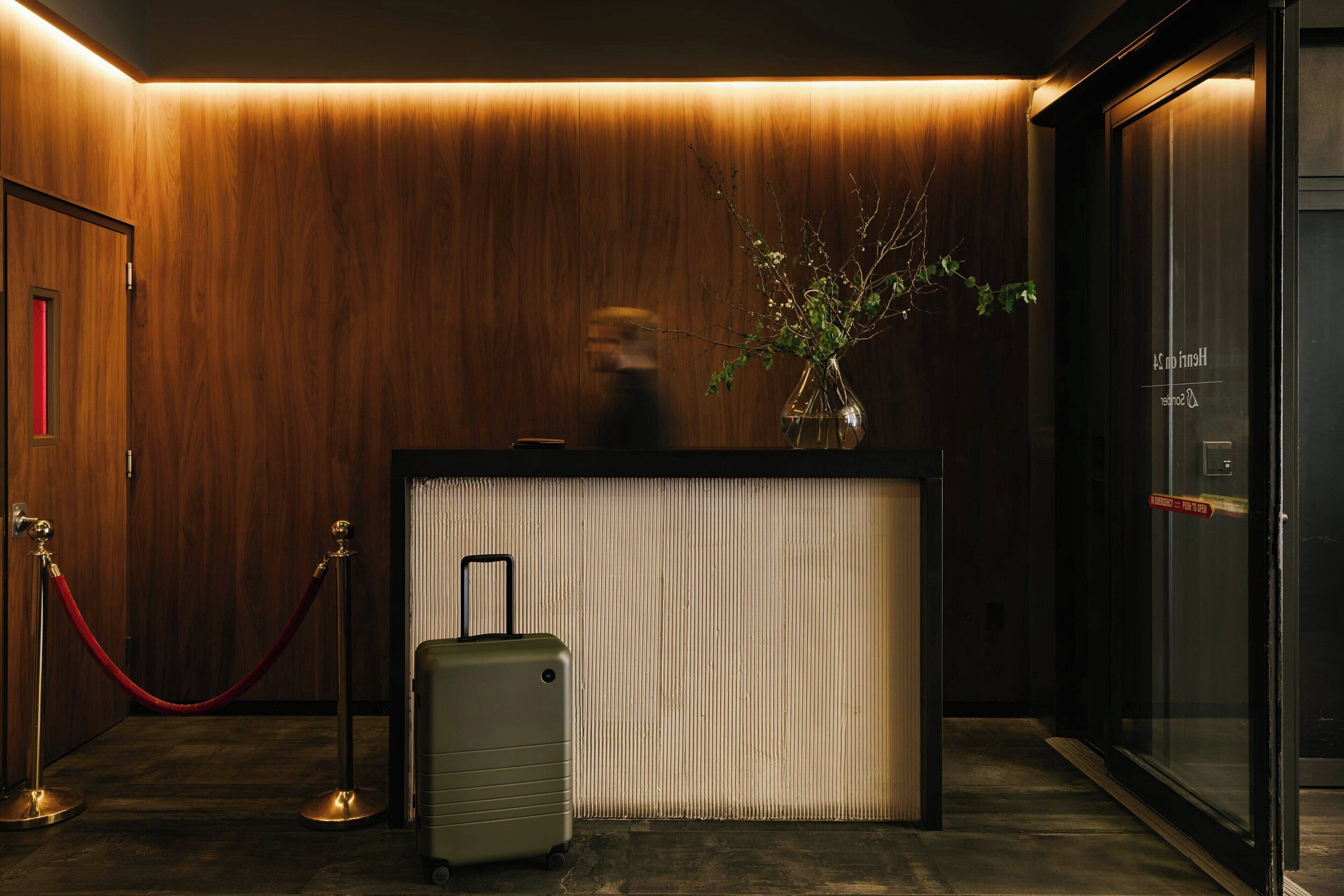 Un área de recepción con un muro de madera, un mostrador de recepción, una barrera de cuerda roja y una maleta.