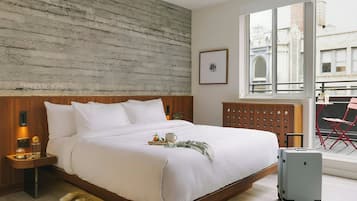 A neatly made bed with pillows and a tray, a suitcase, and a window with a view of buildings.