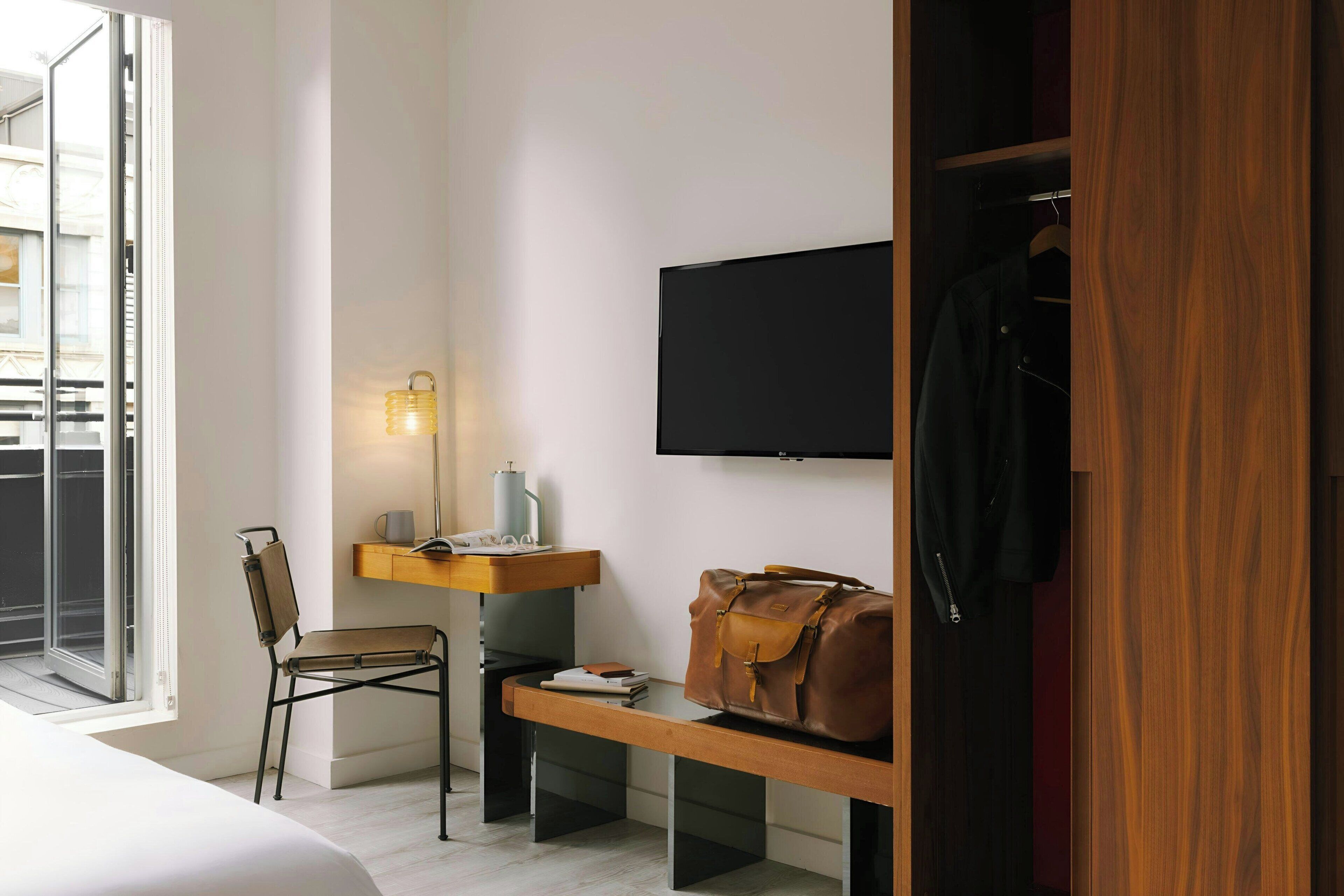 Una habitación de hotel moderna con una cama, un escritorio con lámpara, una silla, un televisor y un armario.