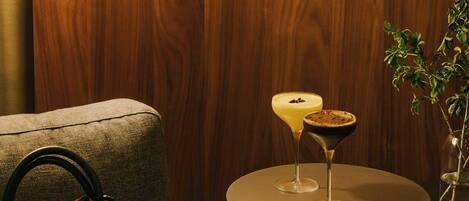 A wooden wall, a round table with two drinks, a lamp, and a handbag on a couch.