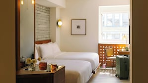 A hotel room with two beds, a desk with a lamp, a chair, a suitcase, and a window with a view. - Hotel Henri NY (New York)