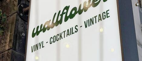 A sign for 'wallflower' with the text 'VINYL - COCKTAILS - VINTAGE' on a white background with green lettering.