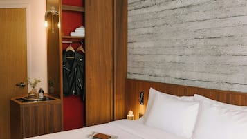 Habitación de hotel con un armario de madera, cama con ropa de cama blanca, pared roja y pared texturizada detrás de la cama.