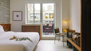 A hotel room with a bed, a desk, a chair, a window with a view of buildings, and a radiator. - Hotel Henri NY (New York)