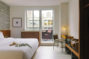 Habitación de hotel con cama, escritorio, silla, ventana con vistas a edificios y un radiador.