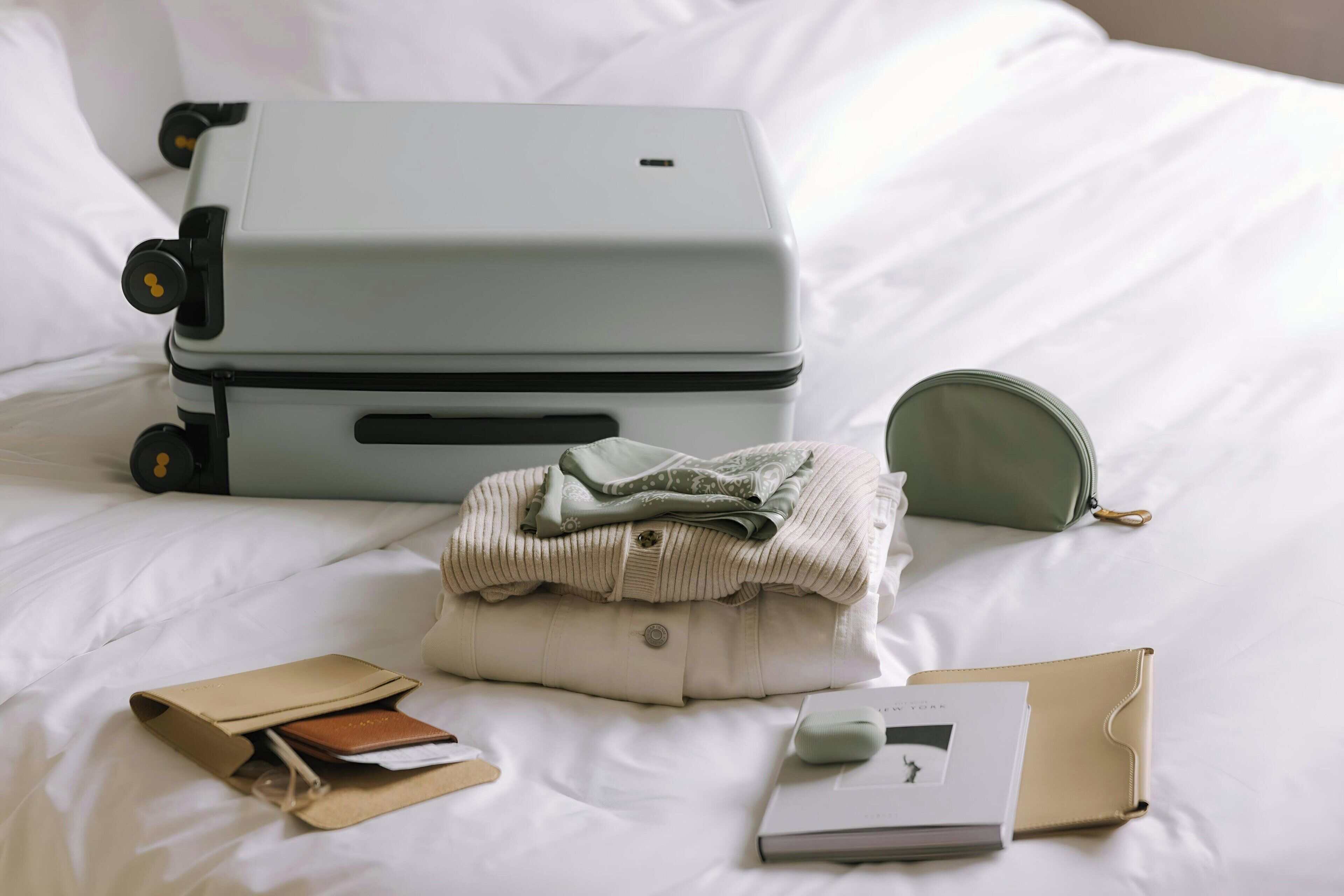 Un lit avec une valise, une veste pliée, un portefeuille, un livre et une paire de chaussons.