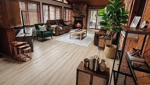 A spacious living room with a fireplace, wooden floors, and large windows.
