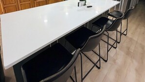 A modern kitchen with wooden cabinets, stainless steel appliances, a white island with bar stools, and recessed ceiling lighting.