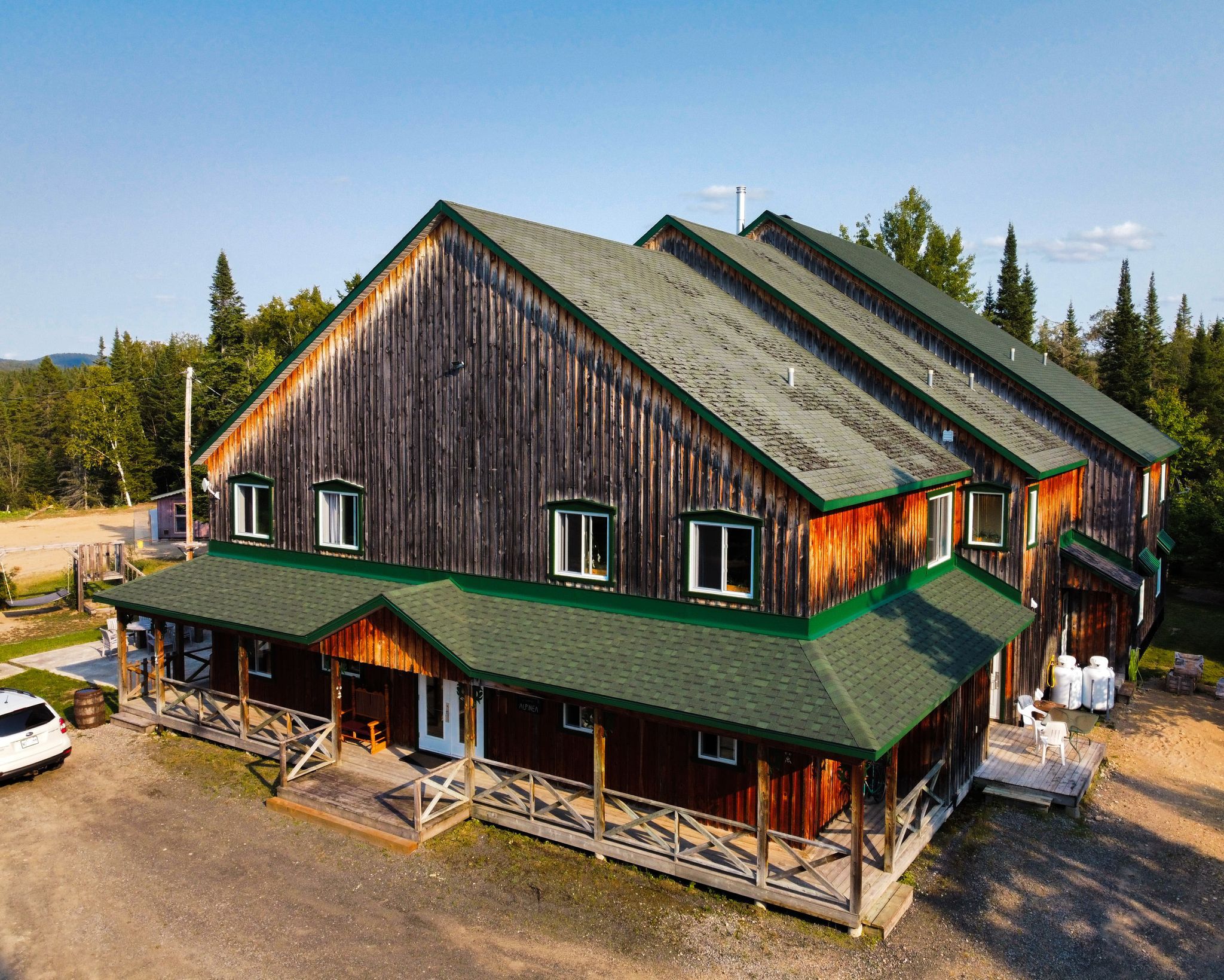 A large wooden building with multiple levels, a green roof, and a covered front porch with outdoor seating.