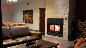 Una sala de estar con chimenea, sofás de cuero, una mesa de centro de madera con piezas de ajedrez, y un comedor con sillas y una mesa.