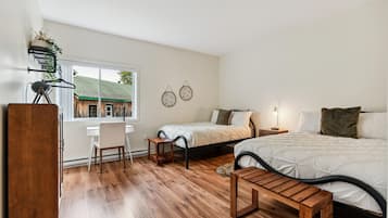 A bedroom with two beds, a desk, and a chair. There is a window with a view of a building outside.