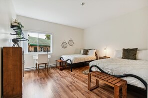 Une chambre avec deux lits, un bureau et une chaise. Il y a une fenêtre donnant sur un bâtiment à l’extérieur.