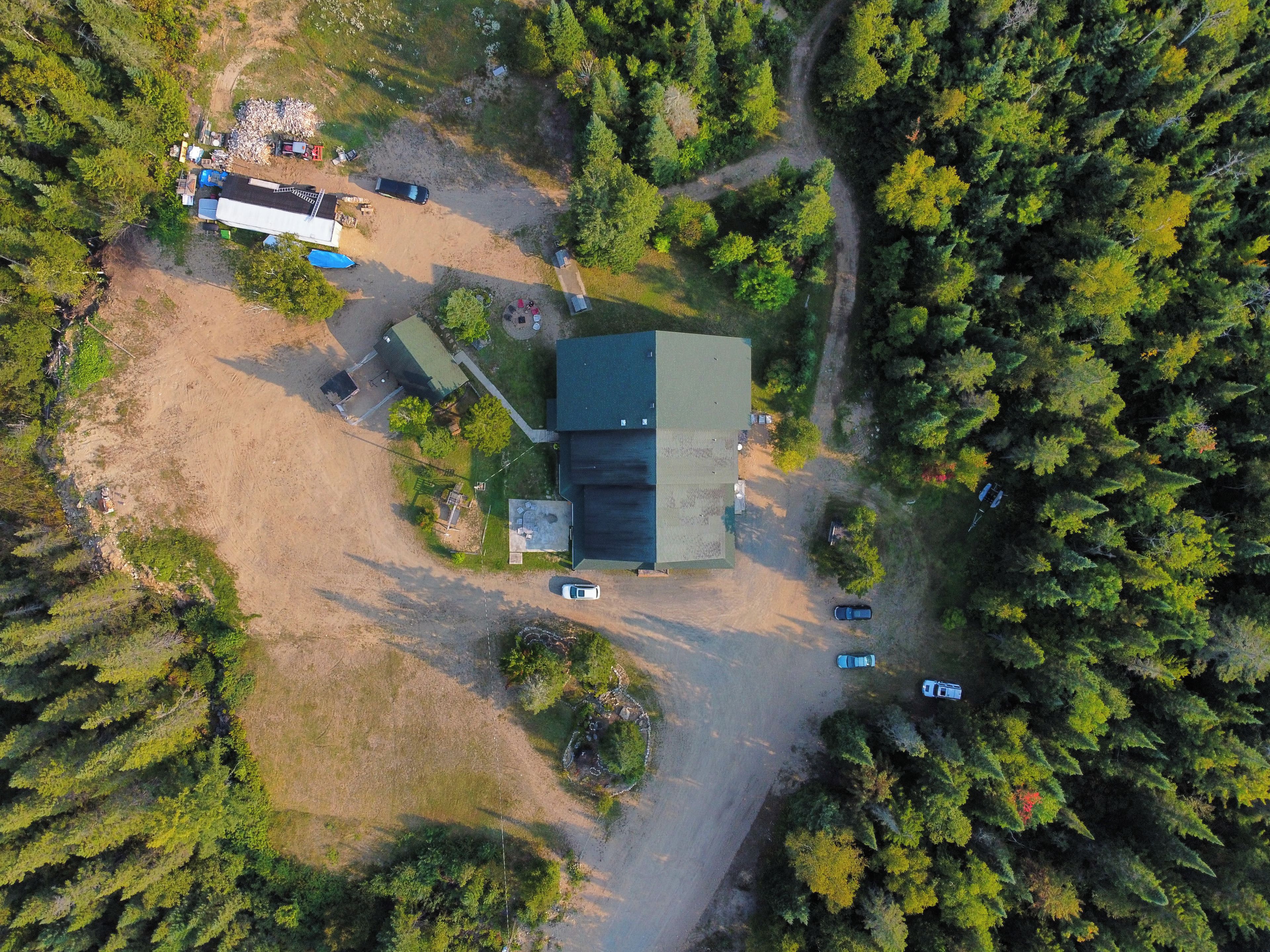 An aerial view of a property with a large building, a parking area, and surrounding forest.