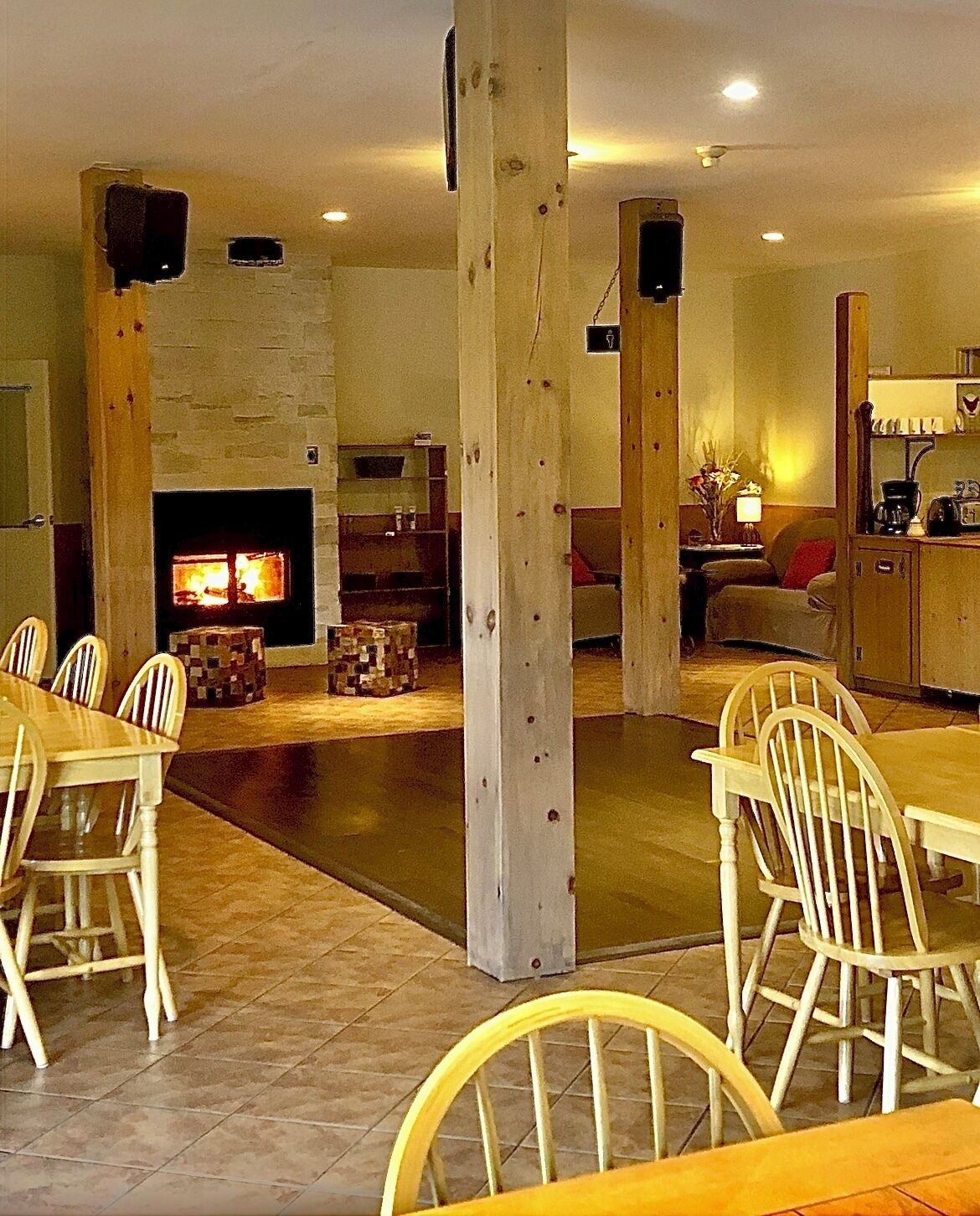 Amplia sala de estar con chimenea, vigas de madera, comedor con sillas blancas y zona de cocina con cafetera.