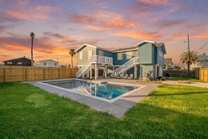Una casa de dos plantas con piscina, cerca de madera y cielo despejado.
