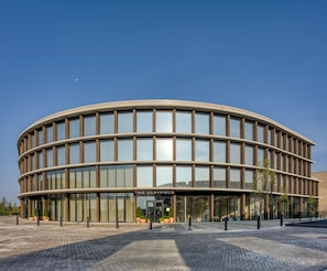 Um edifício moderno e circular com fachada de vidro e uma placa com a inscrição 'The Clayfield'.