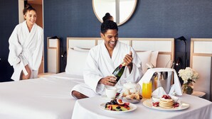 A hotel room with a bed, breakfast setup, and a mirror on the wall.