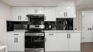 A modern kitchen with white cabinets, a stainless steel stove, a microwave, and a sink.