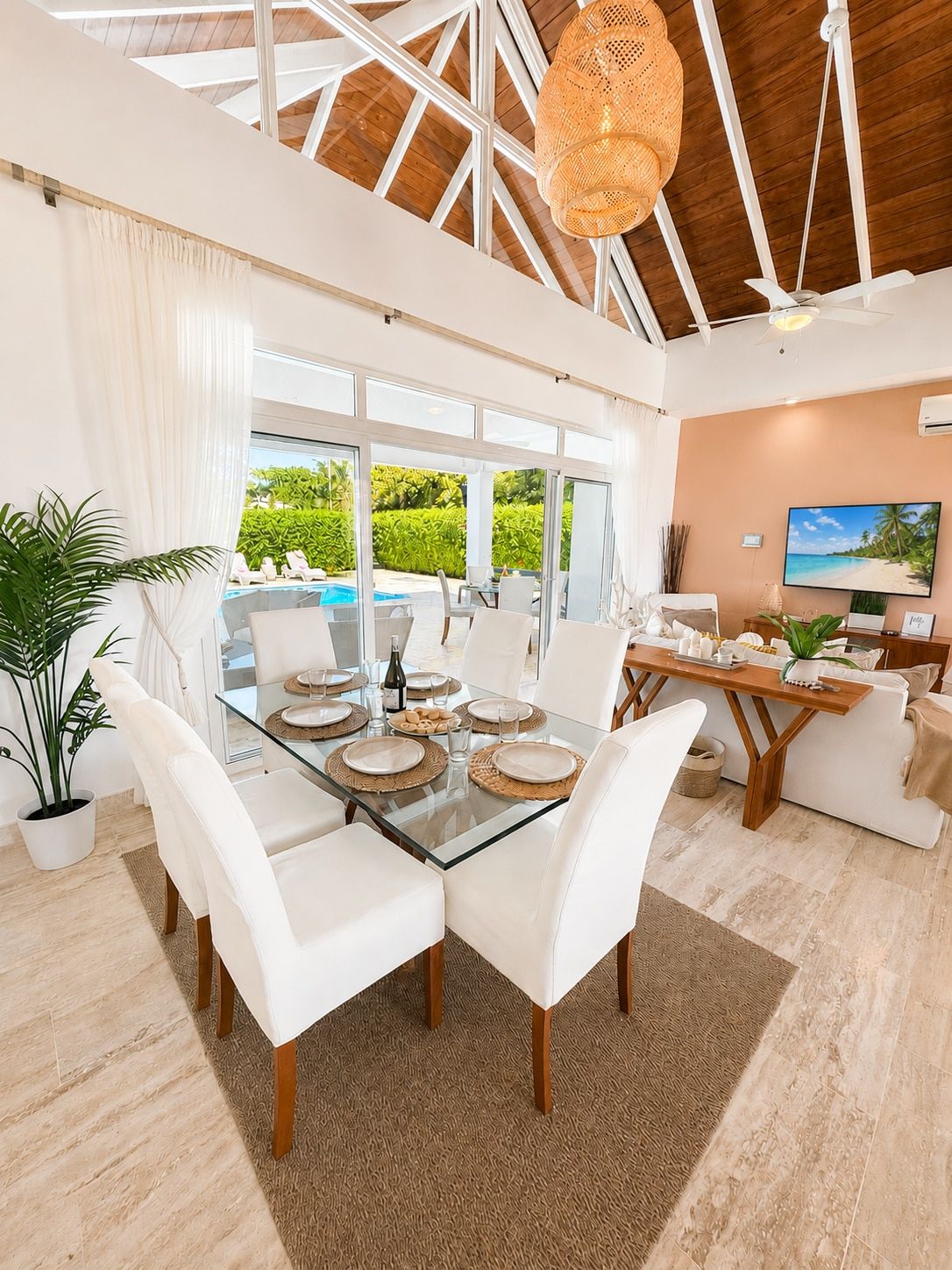 A spacious dining area with a glass table, white chairs, and a view of a pool and greenery outside.