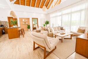 A spacious living area with a wooden ceiling, a kitchen area with a bar, and a seating area with a sofa and chairs. - Ocean View Pool Villa | Walk to 3 Clubhouses (Sosúa)