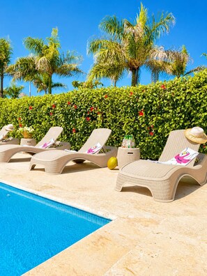 Ein Poolbereich mit Liegestühlen, einer Hecke und Palmen.