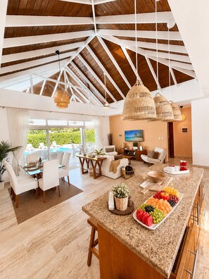 A spacious living area with a high ceiling, a dining table, and a fruit display. - Ocean View Pool Villa | Walk to 3 Clubhouses (Sosúa)