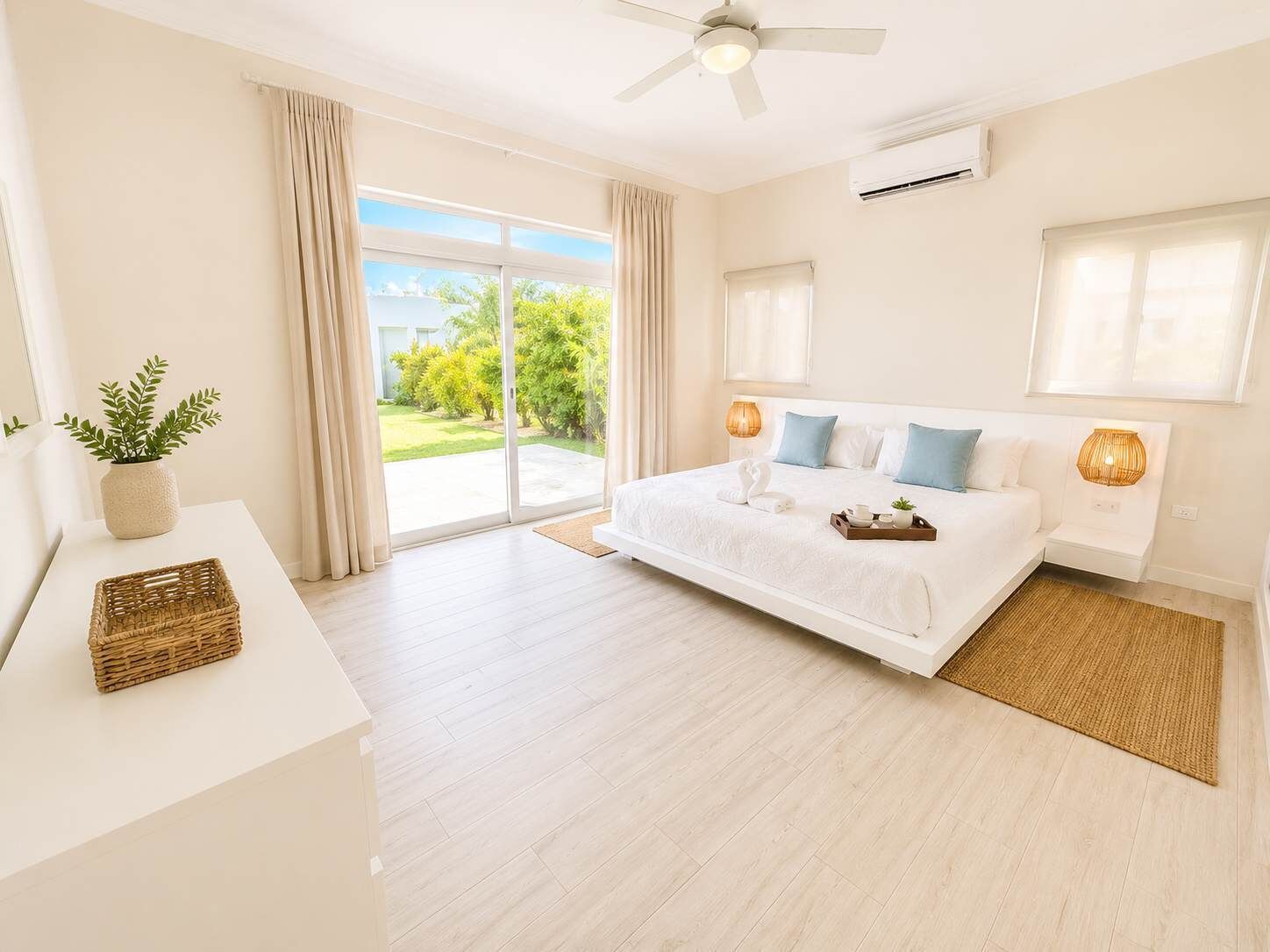 A modern bedroom with a large bed, a ceiling fan, and a view of a green landscape through the sliding glass door.