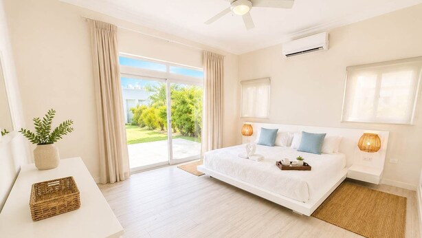 Un dormitorio moderno con una cama grande, un ventilador de techo y vistas a un paisaje verde a través de una puerta corrediza de vidrio.
