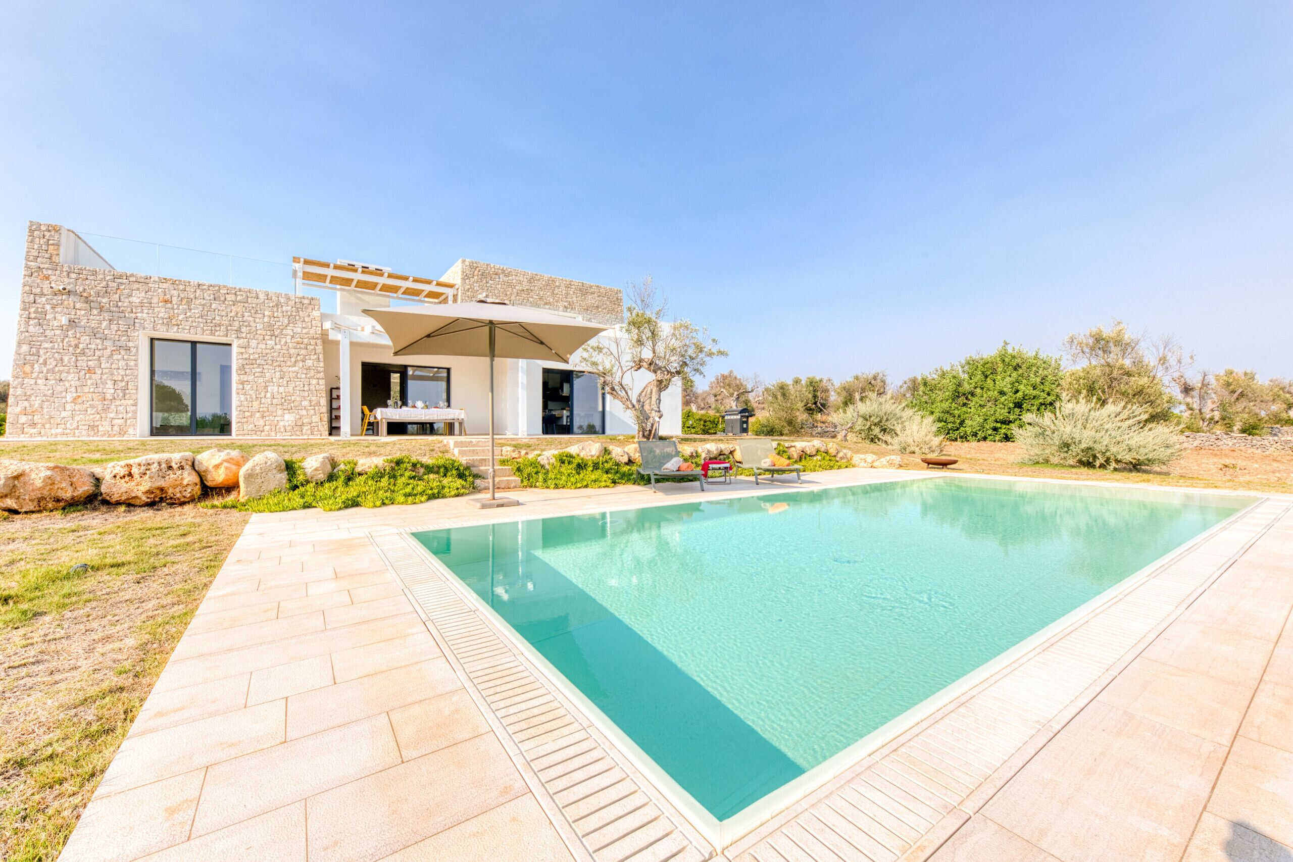 Una casa moderna con piscina, fachada de piedra y zona de estar al aire libre.