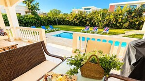 A patio with wicker furniture, a table with a bottle, glasses, and a fruit platter. - Sleeps up to 14 | 4 King Suites & Private Pool (Sosúa)