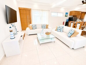 A modern living room with a flat-screen TV, a glass coffee table, and a white sofa set. - 5bd Corner Lot Villa|Private Pool, Sleeps up to 14 (Sosúa)